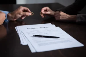 A man and woman holding their wedding bands above a signed divorce decree on a dark desk