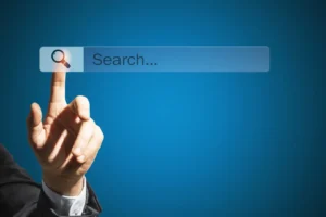A person in a suit pointing a index finger at a translucent search bar with a magnifying glass icon on a blue background.